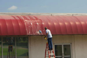 Owner Mike Jackson on a ladder hand scrubbing a commercial owning using a soft-bristled brush.